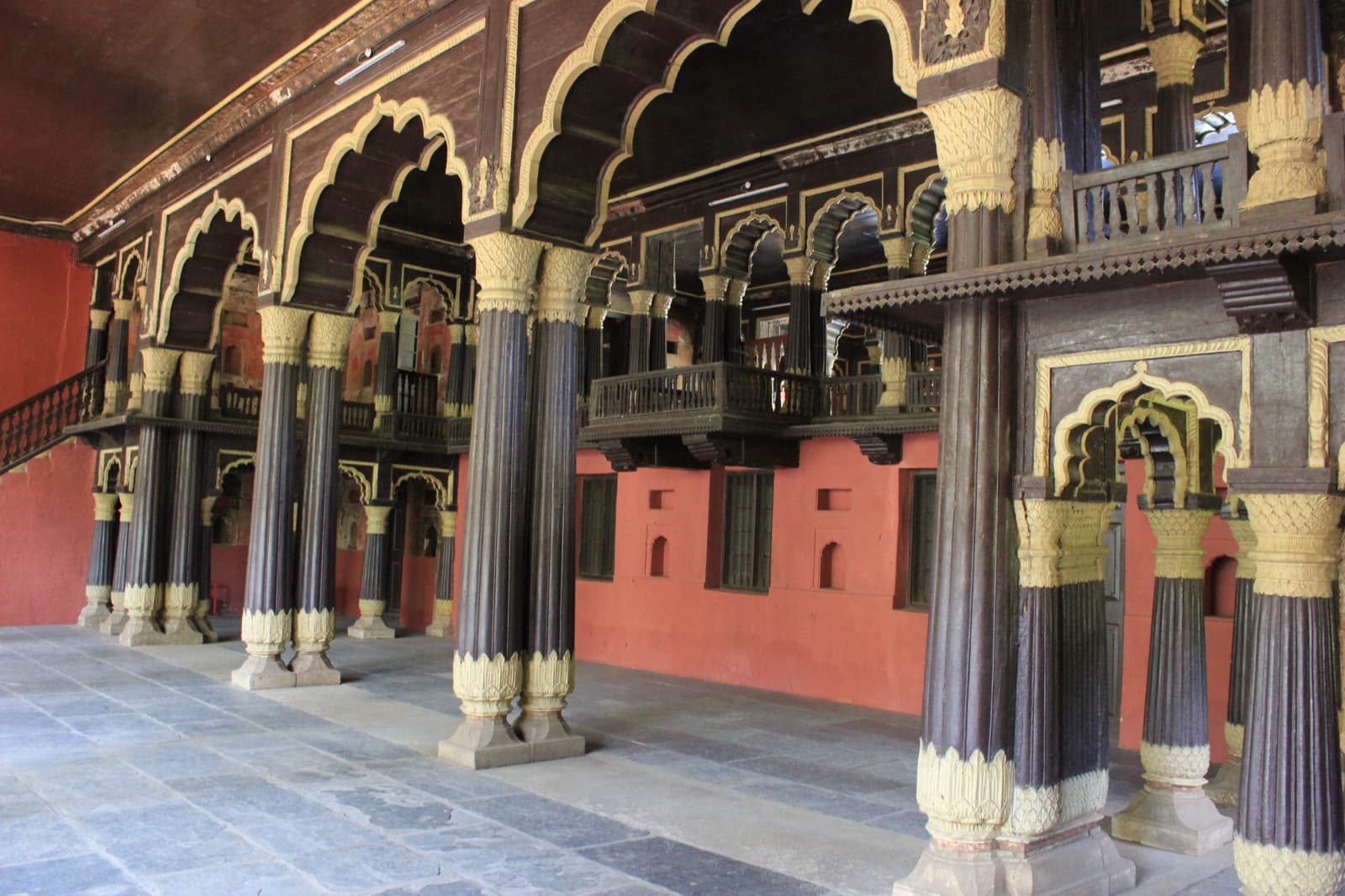 Interior of the Bangalore summer palace: rows of slender teak columns supporting a painted upper gallery.