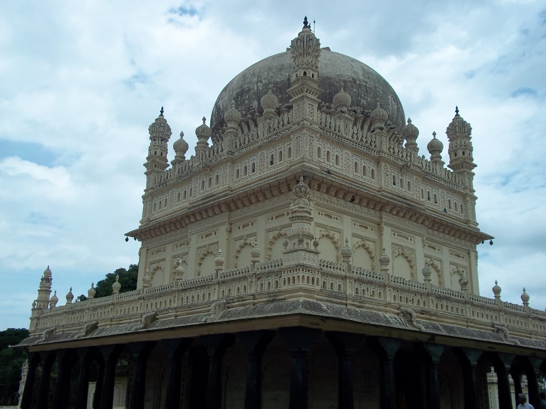 The Gumbaz seen from below: a hemispherical dome, four corner minarets with bulbous finials, and a parapet of small turrets above two tiers of blind arcading.