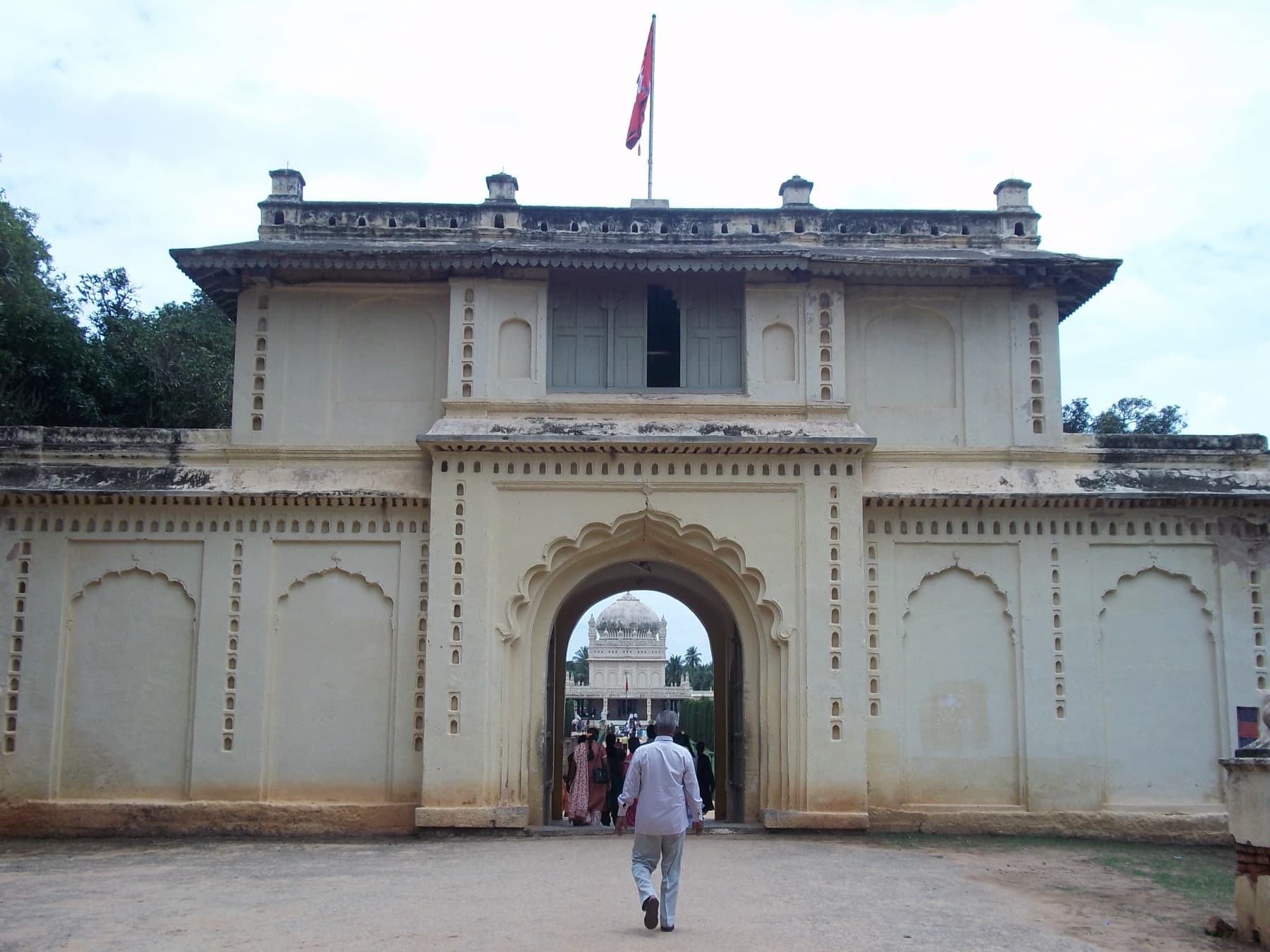 The gateway to the Gumbaz enclosure, with the dome of the mausoleum framed in the archway and visitors walking through.