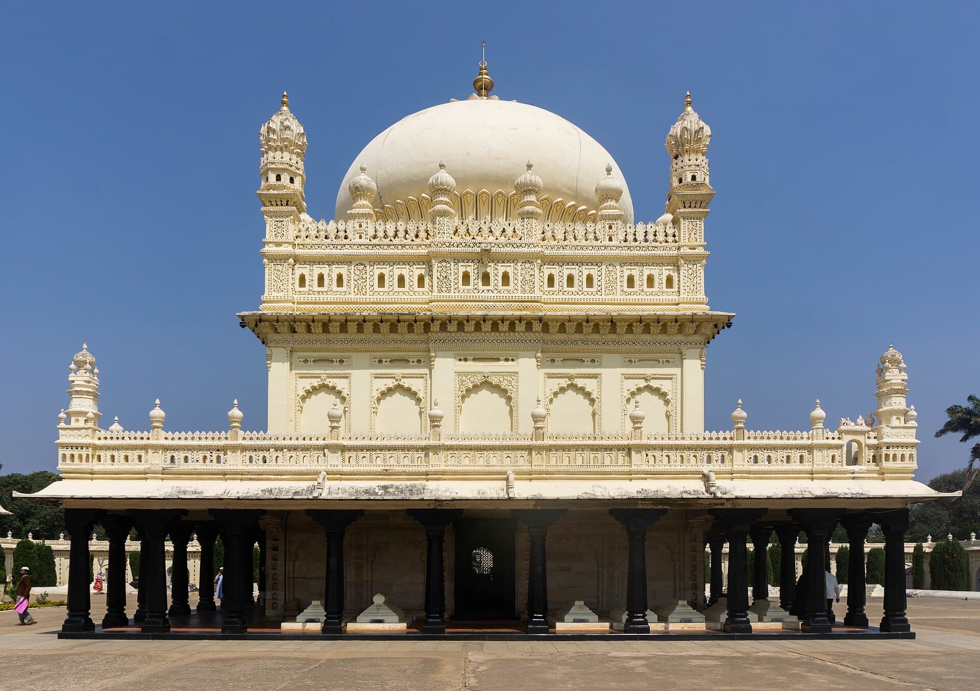 The Gumbaz mausoleum: a white domed tomb on a colonnaded plinth of black pillars under a clear sky.