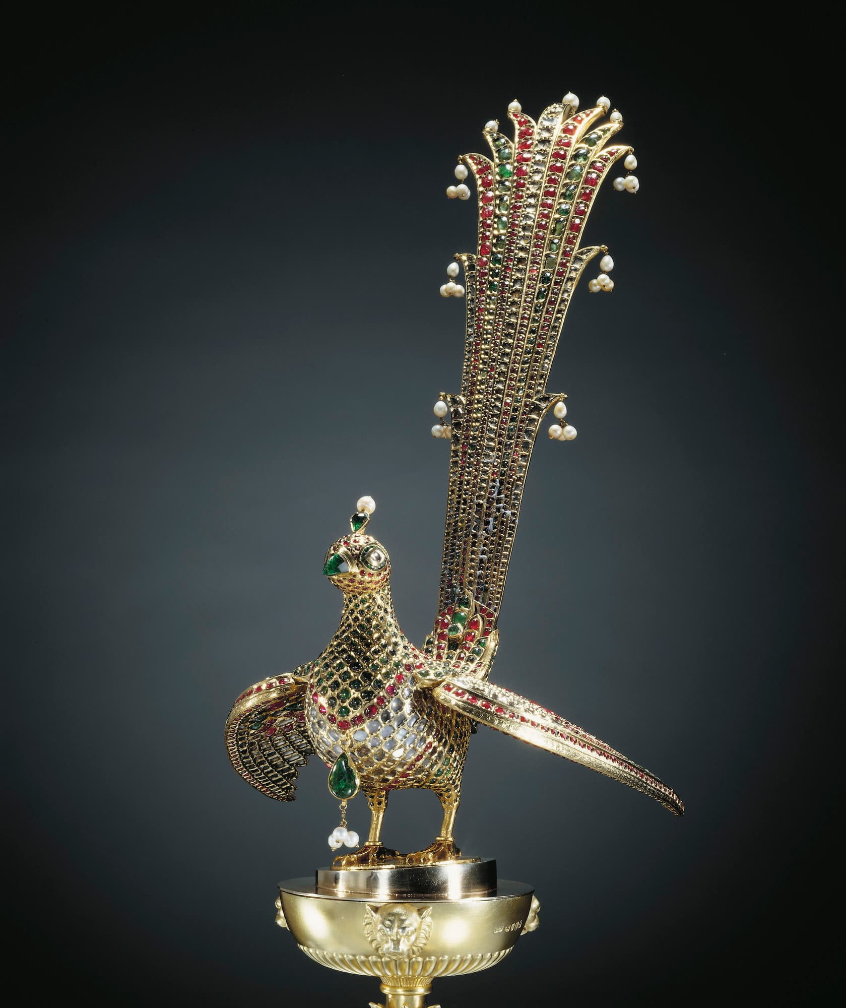 The huma bird from Tipu Sultan's throne: a gold bird entirely covered in rubies, emeralds and diamonds, with a tall fanned tail tipped with pearls, standing on a later gilt cup decorated with tiger heads.