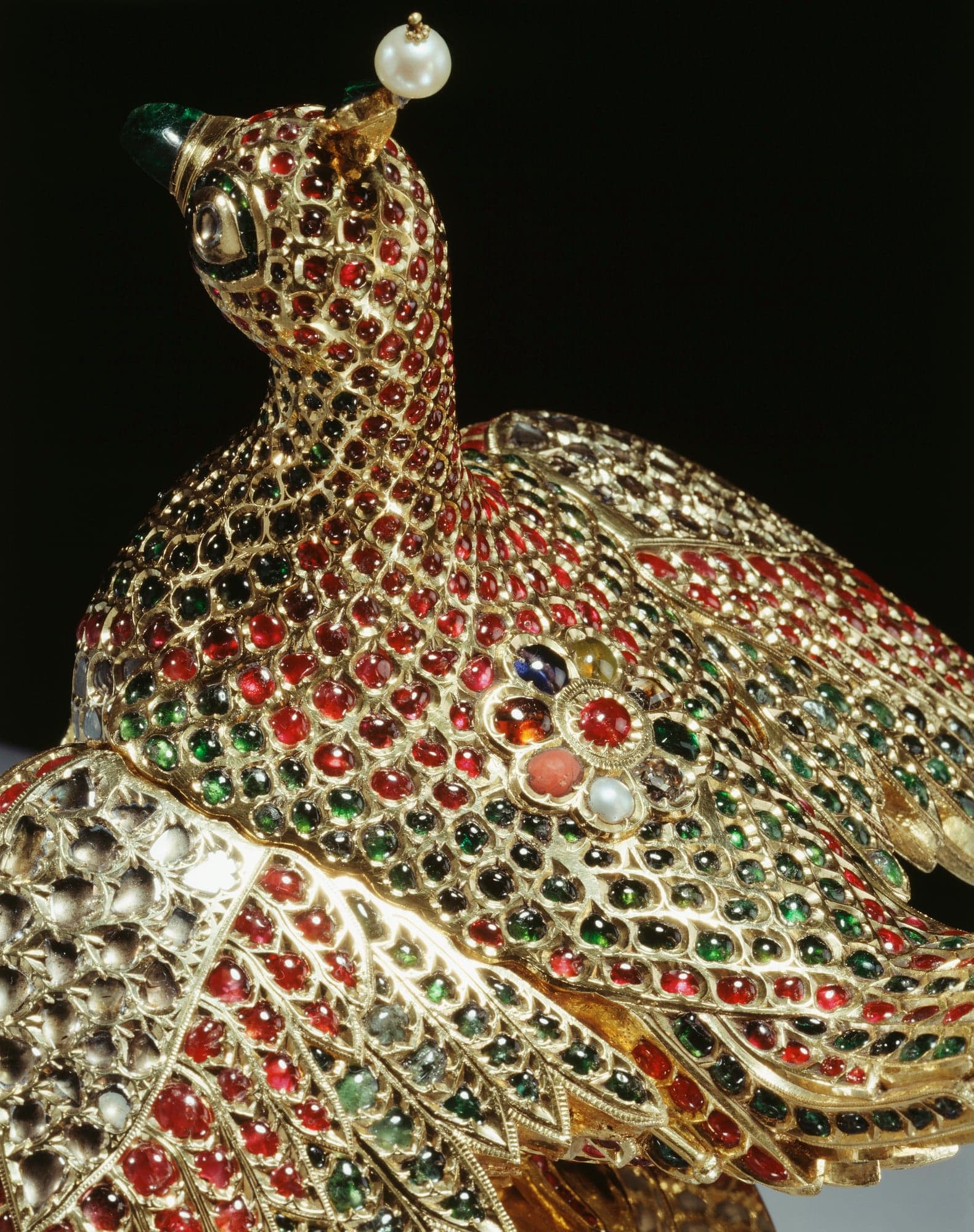 Close view of the huma bird's head and back: gold feathers each set with a ruby or emerald, a pearl-topped emerald crest, and a nine-stone flower of different gems on the shoulder.