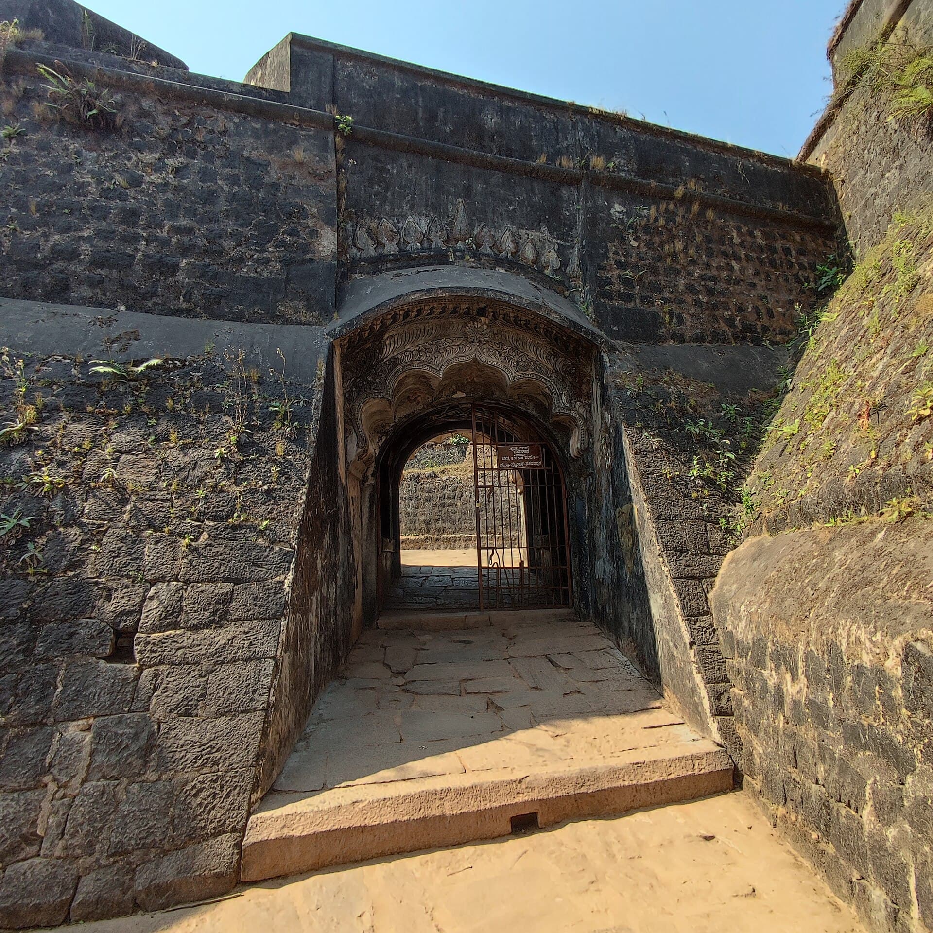 The arched stone gateway of Manjarabad fort, its carved arch set deep in the black rampart wall.