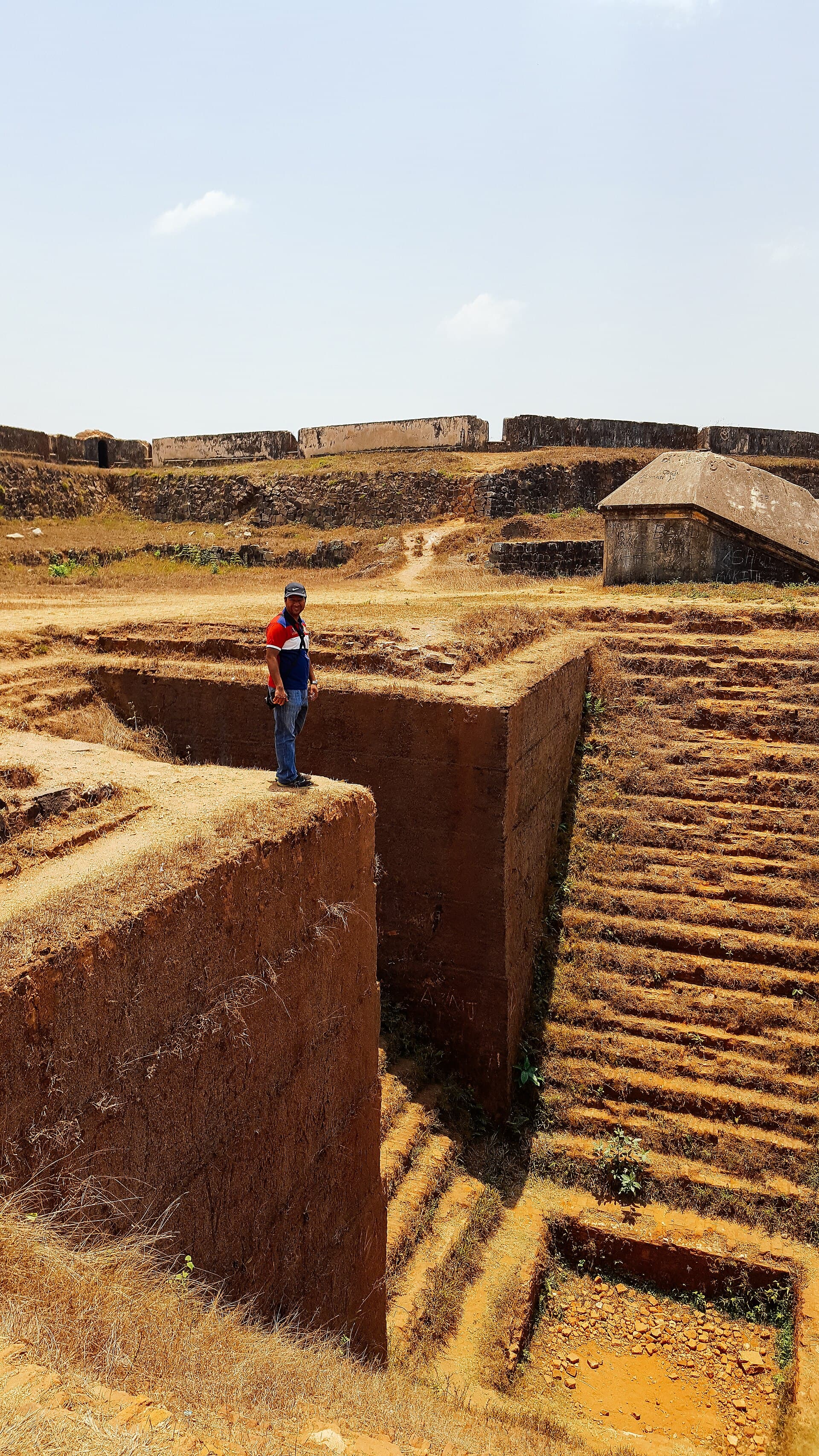 The angular ramparts of Manjarabad fort with a deep dry ditch cut below them, a figure standing on the parapet for scale.