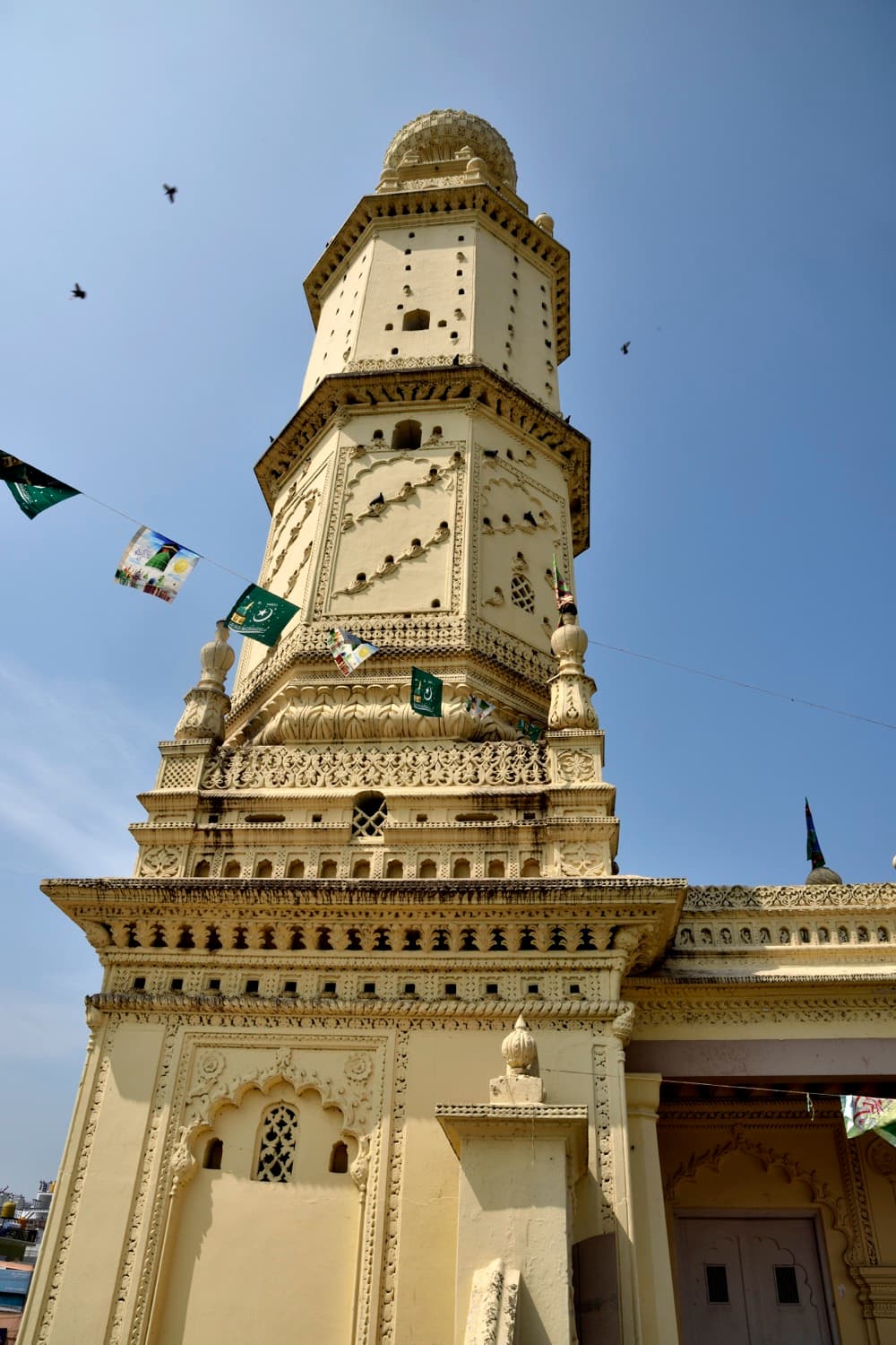 A minaret of the Masjid-i-Ala seen from below: an octagonal shaft rising in stages, each ringed by a projecting balcony, under a ribbed turnip-shaped dome.