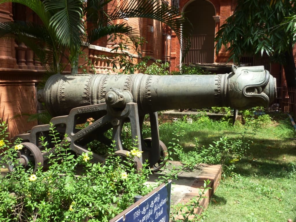 A long Mysorean cannon barrel mounted on a stone plinth outdoors.
