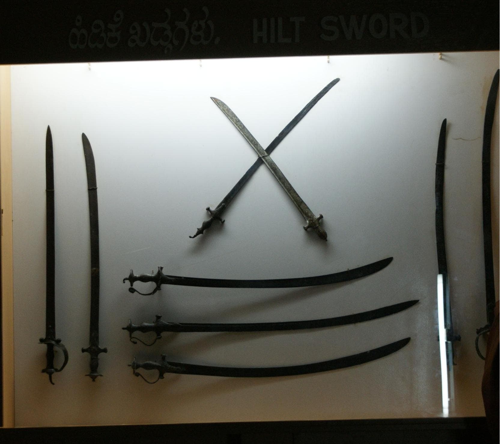 Several curved swords with decorated hilts displayed in a museum case.
