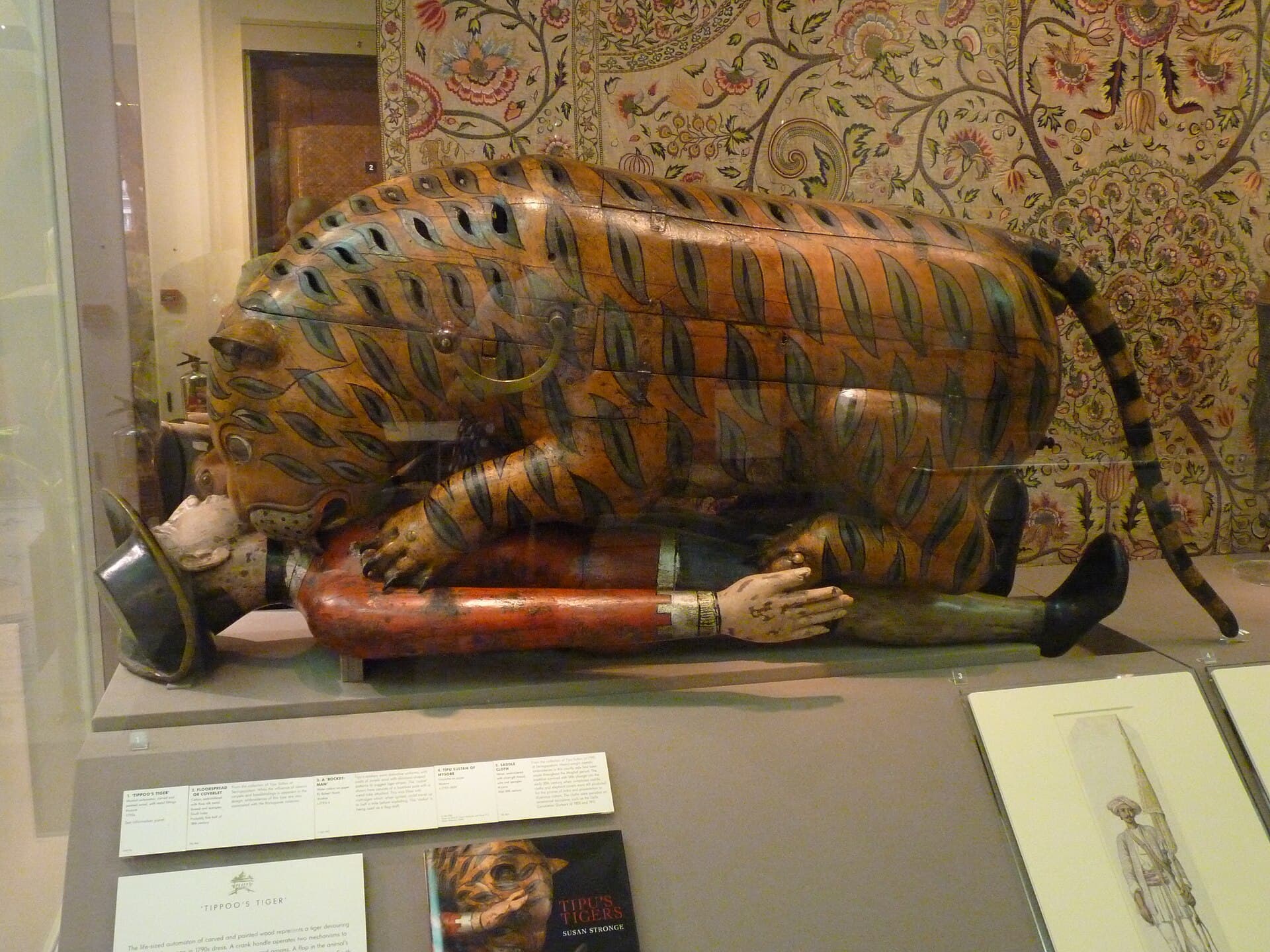 The wooden automaton known as Tipu's Tiger: a painted tiger mauling a prostrate European soldier, displayed in a museum case.