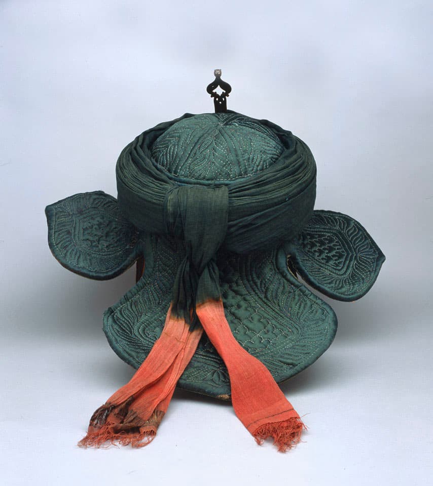 The war turban from behind, showing the green muslin pagri wound round the helmet with its ends, tie-dyed pink, hanging down over the quilted neck flaps.